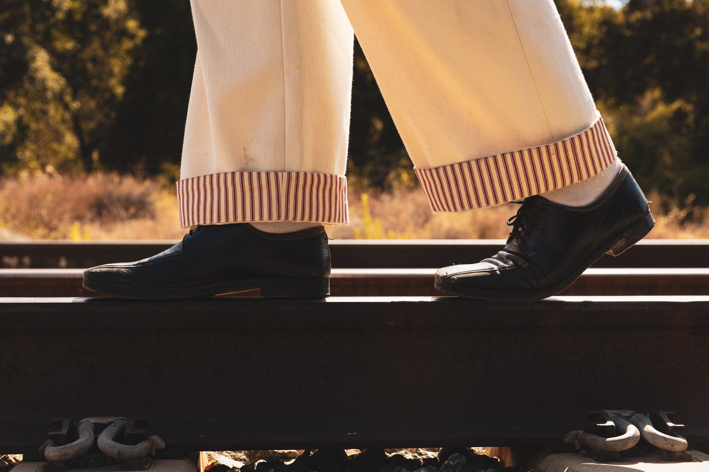 Two cuffed hems resting on a rail, red ticking stripe showing at the turn-up.
